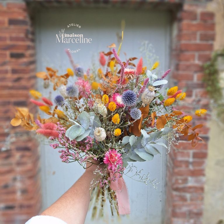 Un bouquet de fleurs séchées colorées avec des accents dorés et un ruban rose.