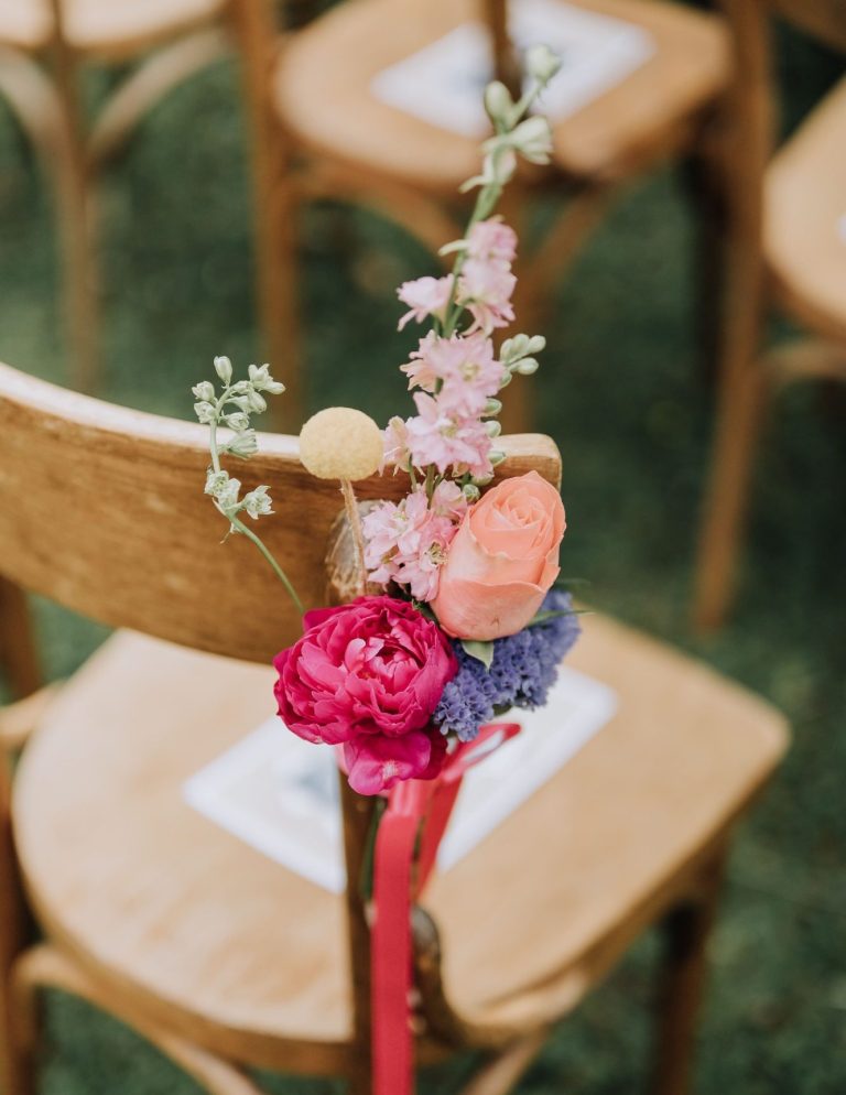 Détails floraux colorés accrochés à une chaise en bois, avec un ruban rose.