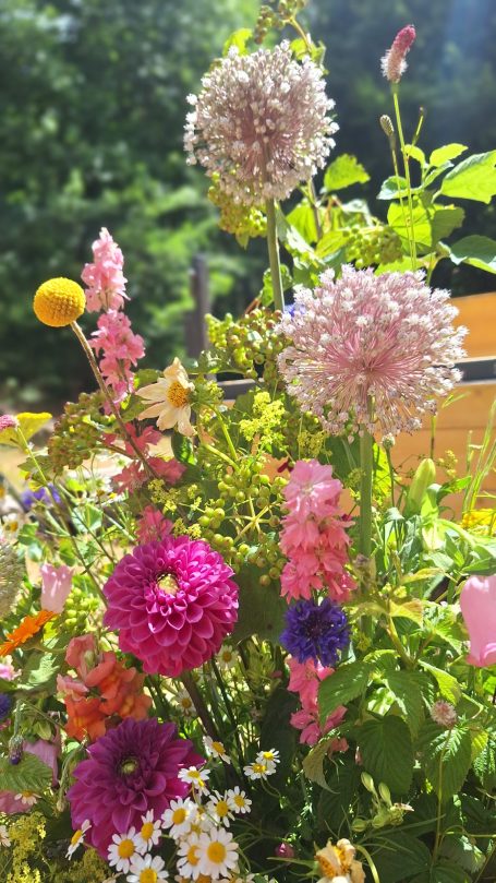 Fleurs colorées en bouquet, incluant des dahlias et des asters, dans un jardin lumineux.