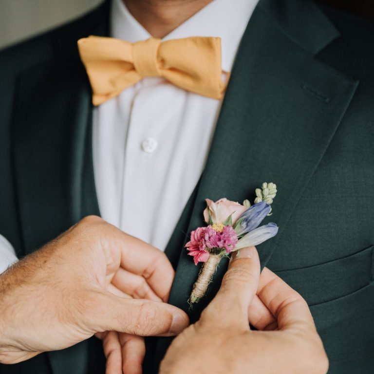 Un homme en costume ajuste une boutonnière décorée de fleurs colorées.
