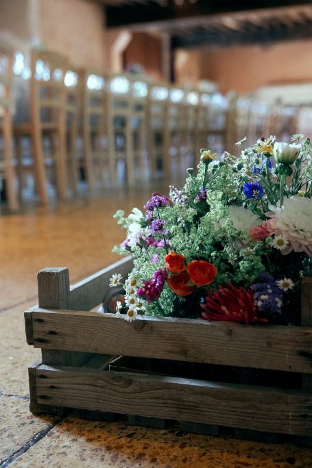 Panier en bois rempli de fleurs colorées, devant une salle avec des chaises en bois.