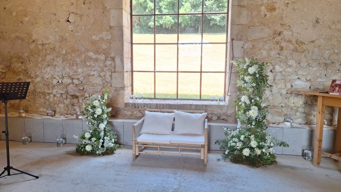 Un coin décoré avec un banc, des fleurs blanches et une grande fenêtre.