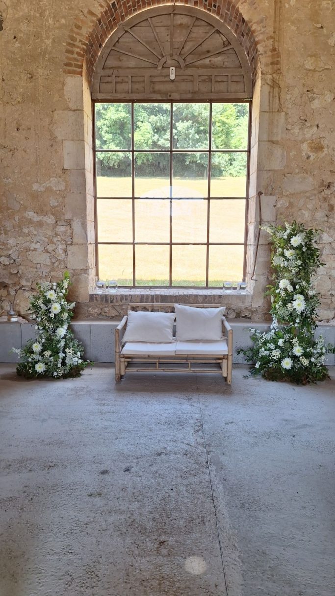 Un banc en bois entre des arrangements floraux dans une pièce lumineuse.