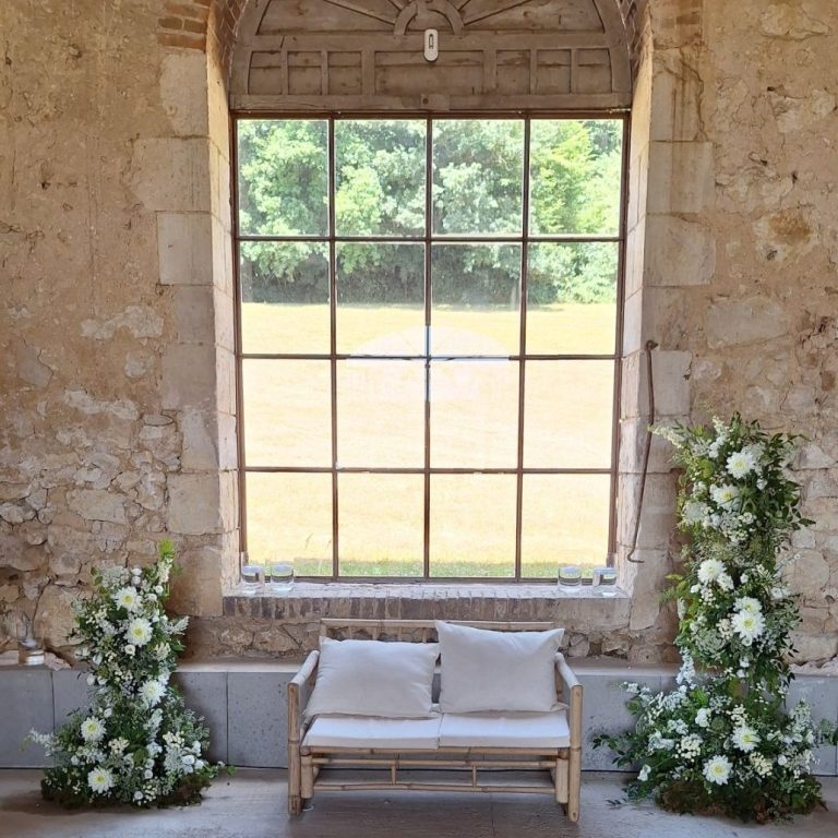 un canapé devant une grande fenêtre, entourée de fleurs blanches.