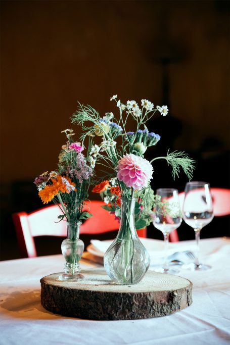 Vases avec des fleurs variées sur une table en bois rustic. Verres en arrière-plan.