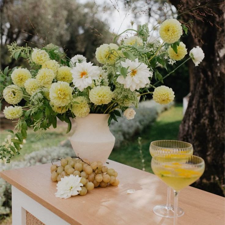 Vase avec des fleurs jaunes et blanches, raisins et deux coupes de cocktail.