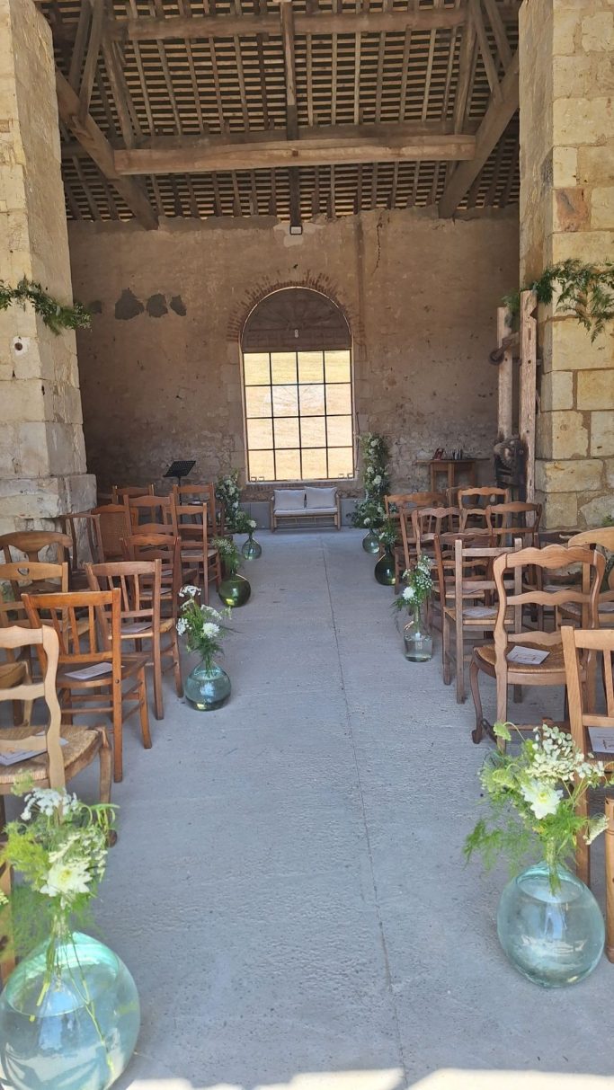Salle de mariage avec des chaises en bois et des vases de fleurs disposés le long du chemin.