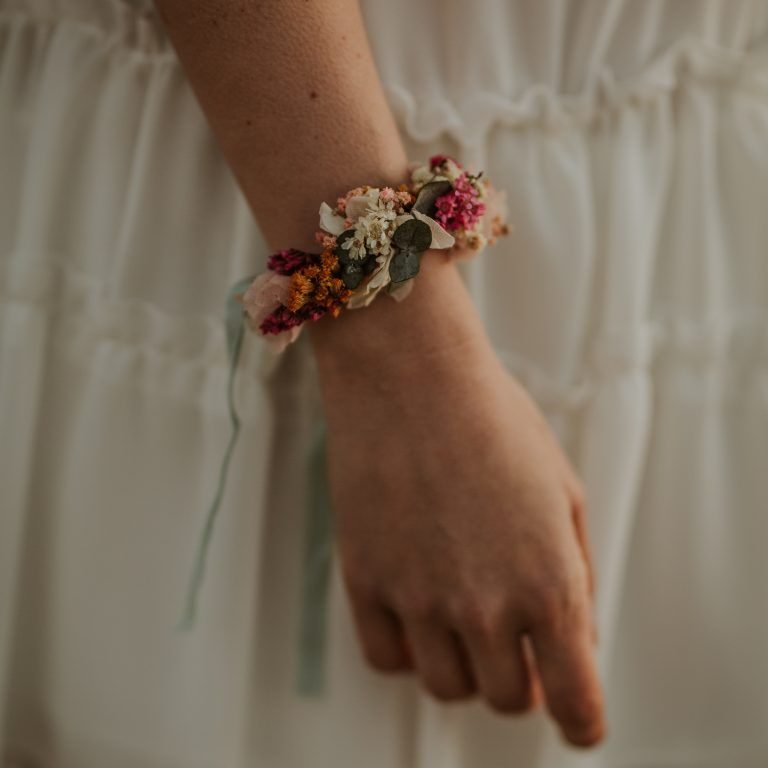 Bracelet floral coloré porté sur un poignet, avec des détails délicats et des rubans.