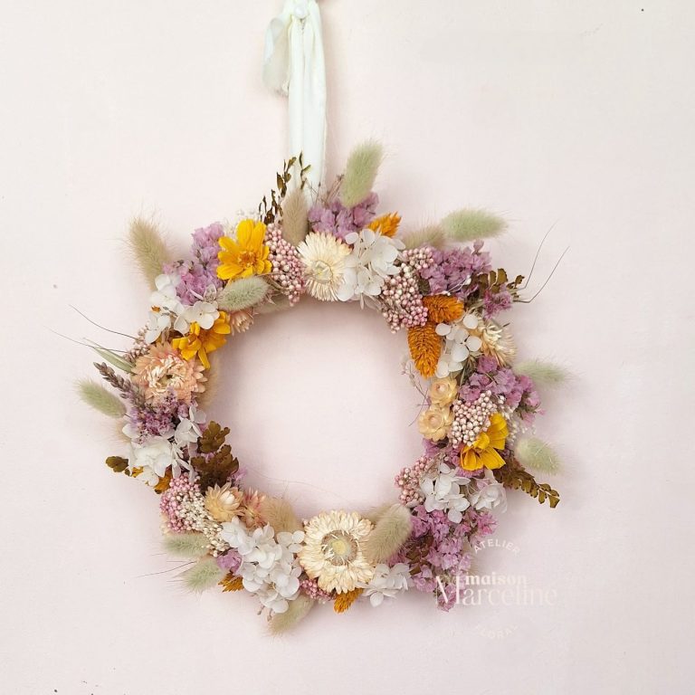 Couronne de fleurs séchées aux teintes douces, accrochée sur un mur clair.