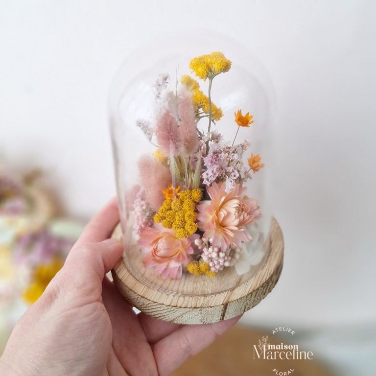 Arrangement de fleurs séchées dans une cloche en verre sur une base en bois.